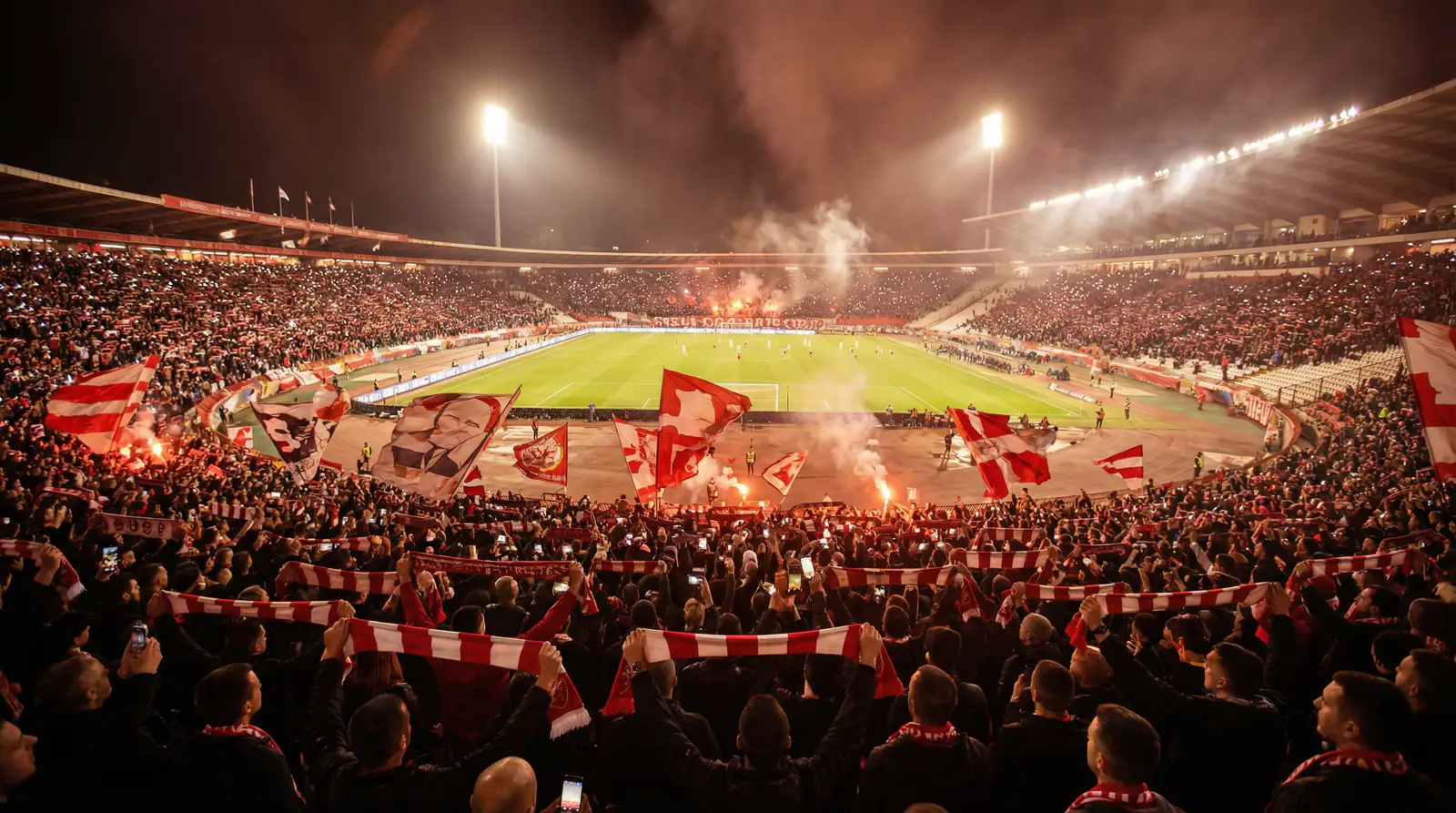 Stadio di calcio pieno di tifosi visto dalla curva durante una partita serale